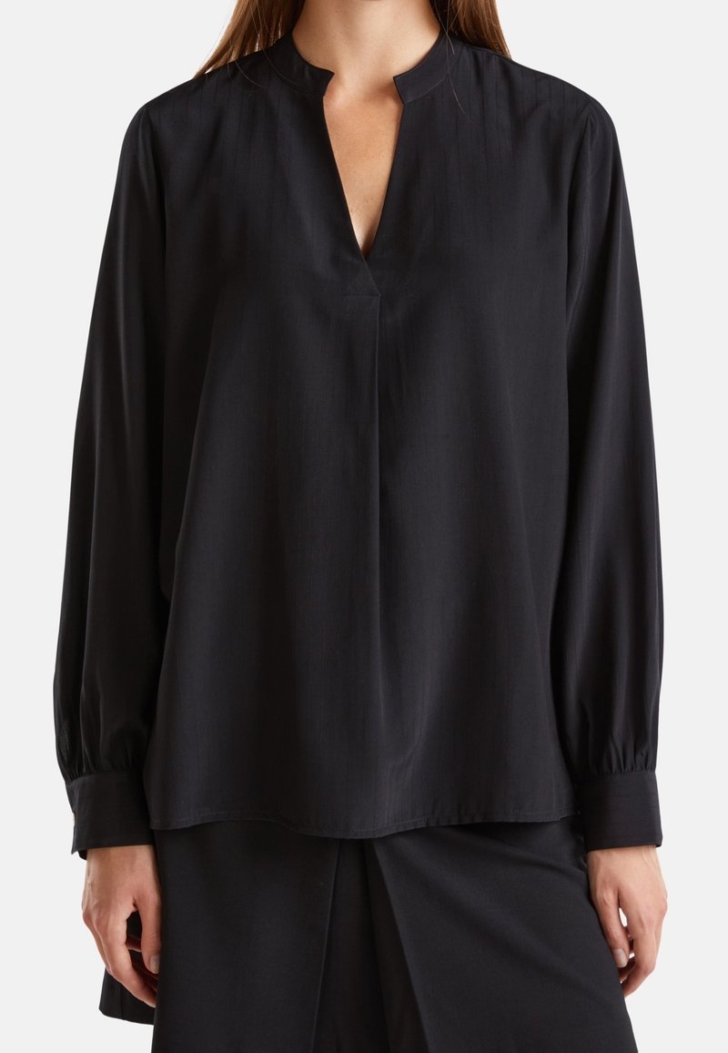 Blouse noire avec un col haut, des manches longues bouffantes et une coupe droite. Tissu lisse, léger avec un éclat subtil.