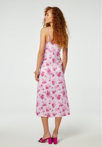 Roze bloemenprint midi-jurk met dunne bandjes, voorzien van een zachte textuur en een losse pasvorm. Gecombineerd met roze hakken.
