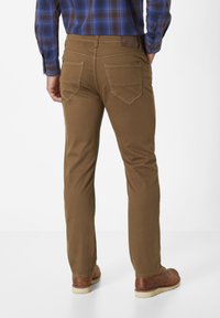 Brown cotton pants with a slim fit, featuring back pockets with triangular flaps and contrast stitching. Worn with brown leather shoes.