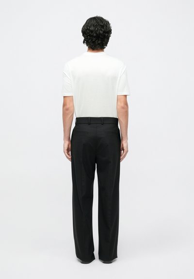 Balta trumpomis rankovėmis marškinėliai, derinami su juodomis kelnėmis, pasižymi tiesiu kirpimu ir lygia tekstūra, matomi iš nugaros.