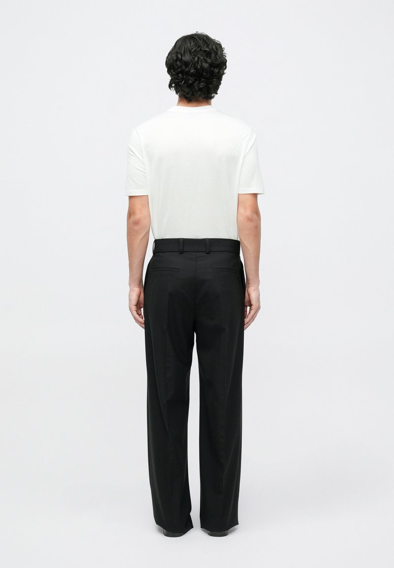 T-shirt bianca a maniche corte abbinata a pantaloni neri, con taglio dritto e tessuto liscio, vista da dietro.
