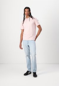 Svetlo roza kratka majica z okroglim izrezom, prilega se postavi, v kombinaciji s svetlo modrimi ravnimi kavbojkami. Model nosi črne superge z belimi črtami.