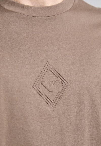 Camiseta marrón de algodón suave; presenta un logo en relieve en forma de diamante. Cuello redondo, diseño minimalista y textura suave.