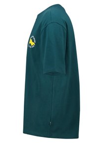 Vihreä puuvillainen t-paita, jossa on lyhyet hihat, pyöreä kaula-aukko ja edessä ja hihassa painettu keltainen graafinen kuva purjeveneestä ja tekstiä.