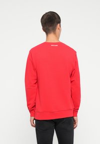 Piros hosszú ujjú pulóver kerek nyakkivágással. A hátsó részen egy kis fehér "PEPE JEANS" logó található a nyaknál. Puha, pamut anyag.