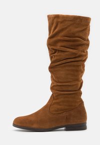 Bottes hauteur genou en daim marron avec un design lâche, un bout arrondi et un talon bas, présentant une texture lisse et des détails de coutures simples.