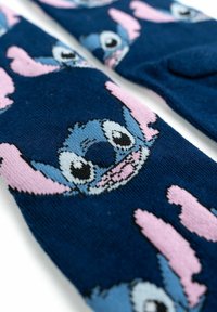 Calze blu in maglia con il volto di un personaggio dei cartoni animati, dettagli in rosa e grandi occhi espressivi, che mettono in risalto un design giocoso.