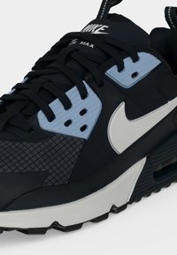 Μαύρο και γκρι αθλητικό παπούτσι Nike Air Max με λευκό σήμα, μαύρα κορδόνια, υφασματικό πάνελ και ορατό αερόσακο στη σόλα.