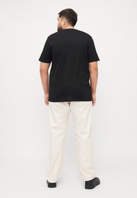 Schwarzes T-Shirt mit kurzen Ärmeln und Rundhalsausschnitt, kombiniert mit off-weißen Hosen. Der Stoff wirkt glatt und hat eine lässige Passform.