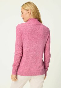 Hellrosa gestrickter Pullover mit hohem Kragen und gerippten Bündchen. Weiche Textur und lässige Passform, mit einem dezenten gesprenkelten Muster.