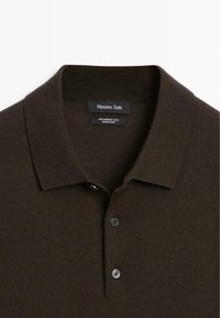 Brown merino wool polo shirt with a classic collar, featuring two buttons. The fabric has a smooth texture and a ribbed design.