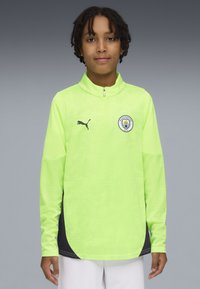 Neon green pitkähihaisen urheilupullovetin, jossa on vetoketju kaulassa, mustia yksityiskohtia ja Manchester Cityn logo rinnassa. Teksturoitu kangaskuvio.