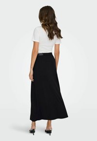 Jupe maxi noire à coupe décontractée, associée à un t-shirt blanc ajusté. Elle présente une texture douce et une ceinture pour un ajustement réglable.