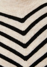 Sweter dzianinowy z wzorem w kształcie litery V, z naprzemiennie ułożonymi paskami w kolorze kremowym i czarnym. Miękka tekstura z prążkowanym dekoltem i szwami.