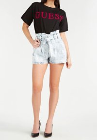 Zwarte katoenen t-shirt met het 'GUESS'-logo in het roze, gecombineerd met hoog getailleerde lichtblauwe denim shorts met een gestrikt taille en versleten details.