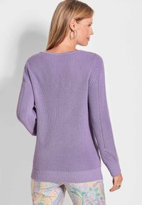 Lila Strickpullover mit langen Ärmeln, gerippten Bündchen und Saum, mit seitlichen Schlitzen und einem strukturierten Muster. Die Rückansicht zeigt einen umfassenden Schutz.