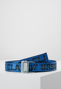 Mėlynas audinio diržas su juodu tekstu, turintis metalinį sagtį. Tekstas sako "CLAS/URBAN." Lygi tekstūra su plokščiu dizainu.
