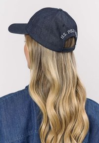 Sötétkék farmer baseballsapka állítható pánttal, hátul fehérrel hímzett "U.S. POLO ASSN." felirattal. Lapos napellenző és formázott kialakítás.