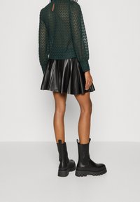 Svarta läderankelboots med tjocka sulor, kombinerat med en svart plisserad kjol och en texturerad mörkgrön stickad tröja med långa ärmar.