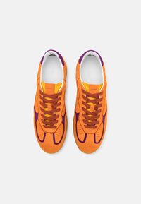 Orange Wildledersneaker mit lila Akzenten, ausgestattet mit einem perforierten Zehenbereich, flachen Schnürsenkeln und einem kontrastierenden gelben Innenfutter.