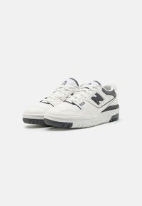 Hvite sportsko med grå detaljer, perforerte sider og en teksturert gummi såle. Har lisser og merkevarelogo på siden.