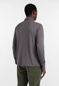 Szara polówka z długim rękawem, z kołnierzykiem i guzikami przy mankietach, wykonana z gładkiego materiału, w zestawie z oliwkowymi spodniami z kordurowej tkaniny.