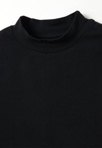 Camiseta de algodón negra con un cuello alto y textura suave. Presenta un diseño sencillo sin patrones ni acentos de hardware.