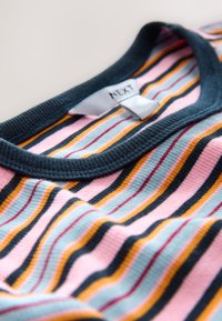 Raidallinen paita, jossa on vaaleanpunaisia, sinisiä, keltaisia ja mustia vaakaraitoja, resorinen tummansininen kaulus ja sisäpuolella "NEXT"-merkki.