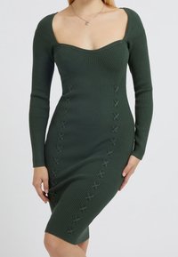 Robe verte en maille côtelée ajustée avec manches longues, encolure carrée, et couture décorative en croix sur les côtés avant.