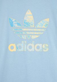 Debeszils t-krekls ar lielu dzeltenu un zilu trīszaru logo un tekstu "adidas" nolietotā, strukturētā fontā. Kokvilnas materiāls.
