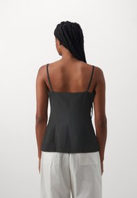 Musthave musta sobiv tank-top õhukeste reguleeritavate rihmadega, struktureeritud disain ja sujuv tekstuur. Kombineeritud heledate laia säärega pükstega.