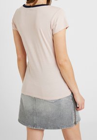 Jasnoróżowa koszulka z krótkim rękawem i granatowym kołnierzykiem, zestawiona z szarą spódnicą dżinsową z bocznym zamkiem i przednimi kieszeniami.