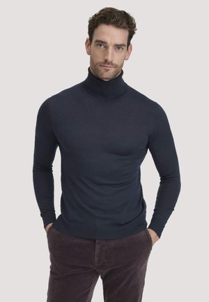 Navyblaue Rollkragenjacke mit glatter Textur, eng anliegendem Schnitt und gerippten Details am Kragen und den Bündchen, kombiniert mit dunklen Cordhosen.