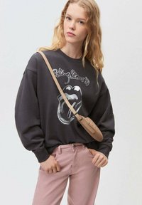 Mörkgrå sweatshirt med en Rolling Stones-grafik, i kombination med rosa byxor och en brun crossbody-väska med perforerade detaljer.