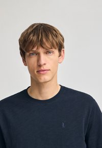 Sweatshirt bleu marine à col rond en tissu doux, avec un petit logo brodé sur la poitrine gauche et un col à côtes.