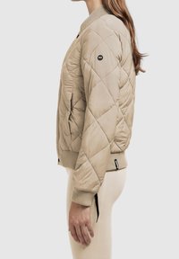 Beżowa pikowana kurtka bomber z prążkowanymi mankietami i kołnierzem. Posiada małe czarne logo na rękawie oraz smukły, dopasowany krój.
