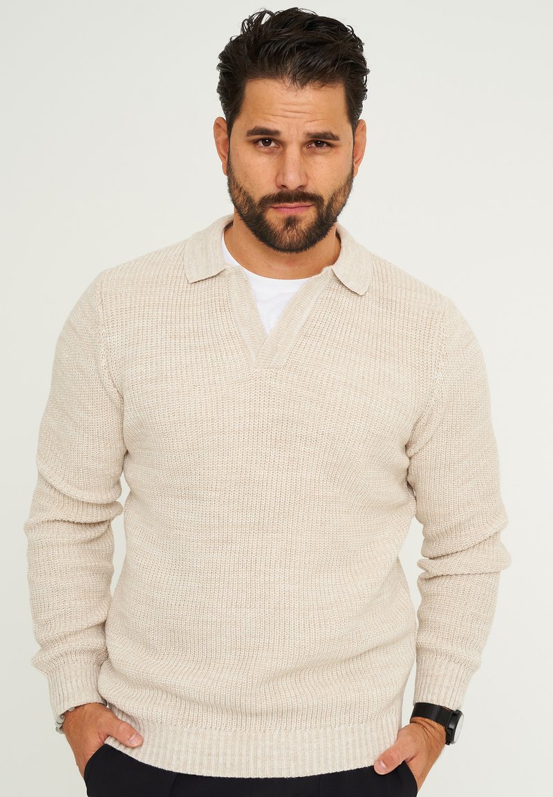 Beige gestrickter Pullover mit strukturiertem Finish, ausgestattet mit einem Kragen und einem V-Ausschnitt. Lange Ärmel und gerippte Bündchen runden das Aussehen ab.