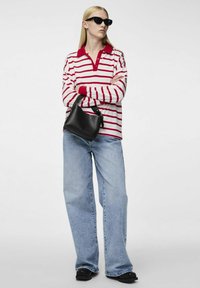 Polo de manga larga a rayas en colores rojo y blanco, combinado con unos pantalones vaqueros de pierna ancha en azul claro y accesorios negros, incluyendo un bolso pequeño y gafas de sol.