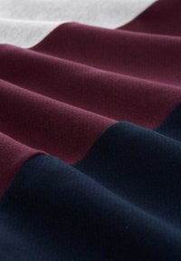 Tessuto con pieghe ondulate in strisce di blu scuro, marrone e bianco. La texture del materiale appare morbida e tessuta con una leggera lucentezza.