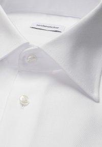Col de chemise blanche avec deux boutons blancs fermés, montrant une petite étiquette en tissu avec le nom de la marque "seidensticker".