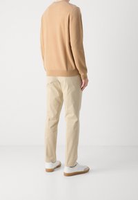 Pullover beige leggero con maniche lunghe, abbinato a chinos beige chiaro. Footwear con sneakers bianche e beige. La texture appare liscia.