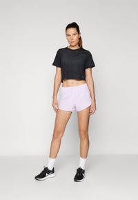 Melna sporta blūze ar īsām piedurknēm, ar sietiņu tekstūru. Gaiši purpursarkani šorti ar elastīgu jostasvietu. Melni sporta apavi, balti potīšu zeķes.