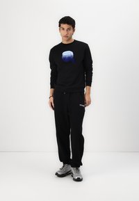 Black sweatshirt with a blue graphic, paired with black sweatpants, and silver athletic shoes with black accents. Plain background.