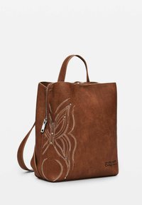 Zaino in pelle marrone con chiusura a zip, caratterizzato da cuciture decorative bianche e ornamenti, contrassegnato da un logo del marchio sul lato.