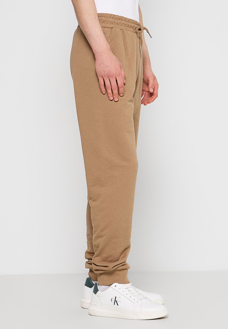 Pantaloni della tuta color beige realizzati in un tessuto morbido, con vita elastica e cordino regolabile. Presentano tasche laterali e polsini a coste.