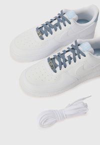 White Nike Air Force 1 sneakers with textured fabric, perforated detail, blue and white patterned laces, and an extra white lace included.
