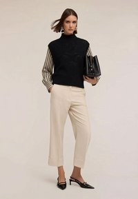 Svart stickad ärmlös polotröja över en randig blus, kombinerad med krämfärgade vida byxor och svarta slingbacks med spetsig tå.