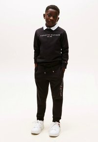 Juodas džemperis su logotipu ir baltu apykakle, derinamas su juodomis sportinėmis kelnėmis, kuriose yra logotipo detalė. Užbaigta baltais sportbačiais.