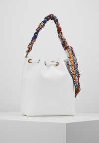 Vit läderhinkväska med guldfärgad öljett och ett färgglatt tyghandtag som är tryckt med flerfärgade bokstäver och mönster.