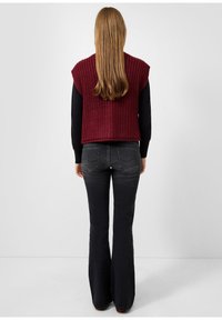 Adīts bordo bezpiedurkņu topiņš, kas savienots ar melnajām platām biksēm. Topiņam ir teksturēta apdare, savukārt bikses ir ar aizmugurējām kabatām.